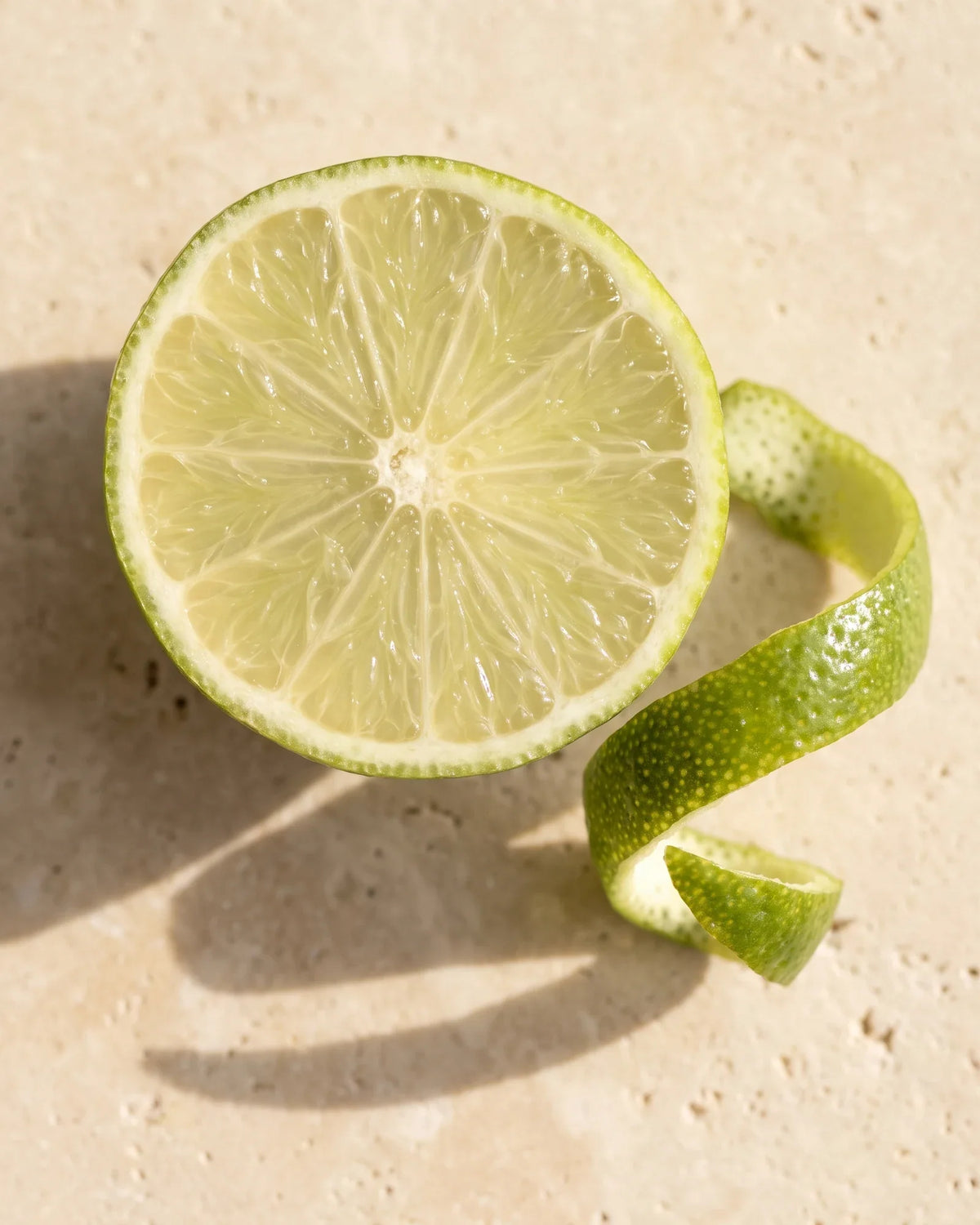 Un limón fresco partida a la mitad y un rizo de ralladura vistos desde arriba sobre travertino cálido: el aroma intenso y fresco del Aceite esencial puro de limón de Delune