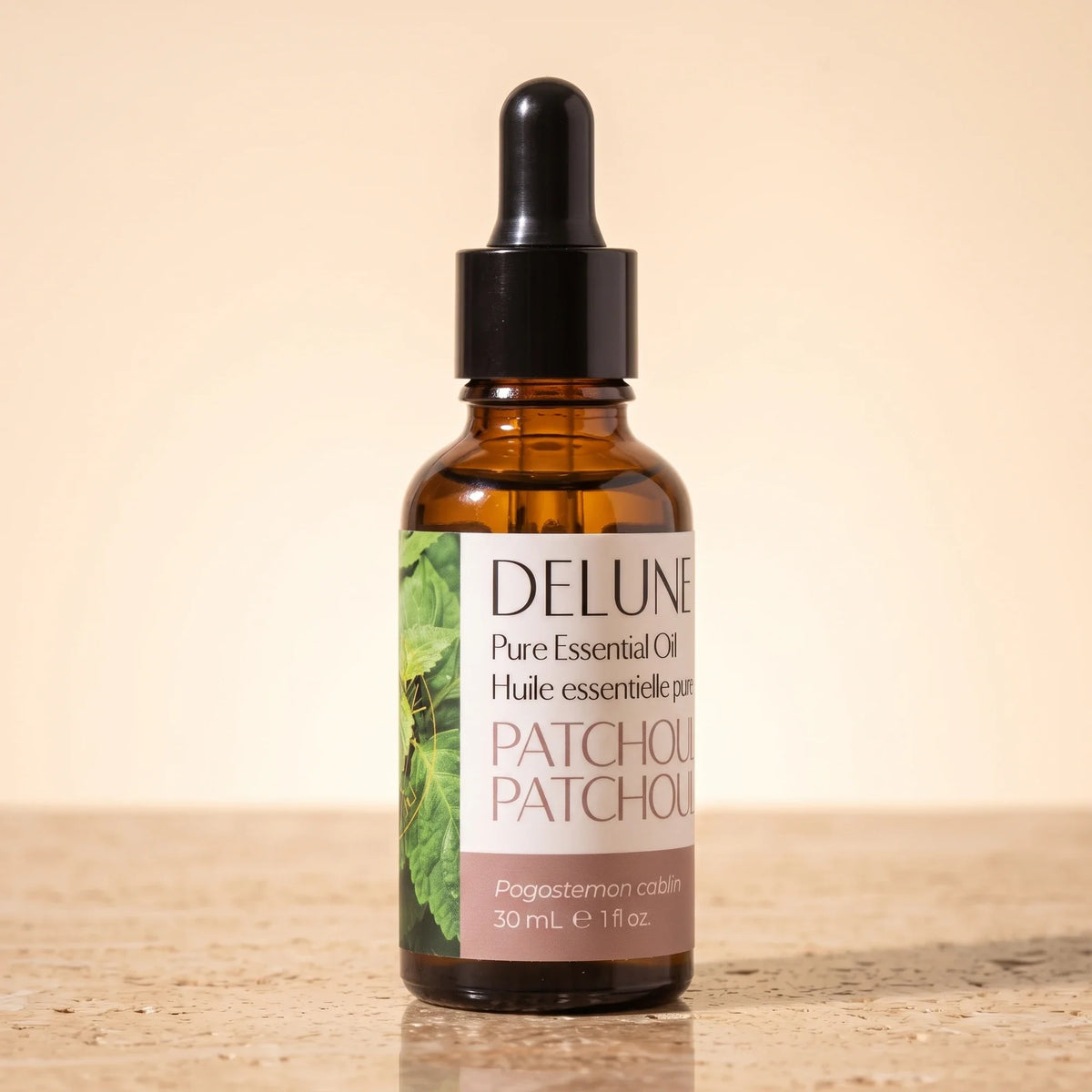 Delune Patchouli Pure Essential Oil, 30ml amber glass dropper bottle on warm travertine stone