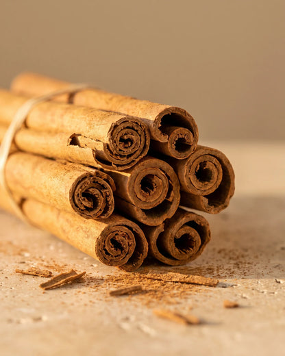 Un manojo de rajas de canela con un poco de canela molida sobre travertino: el aroma dulce y especiado del aceite esencial puro de canela de Delune