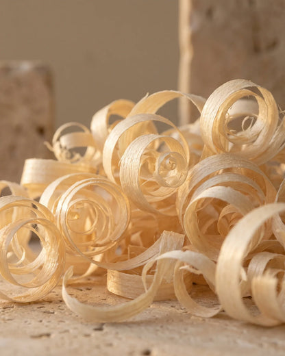 Delicadas virutas de madera de ho clara que brillan a contraluz con una luz cálida: el aroma suave, floral y amaderado del Aceite esencial puro de madera de ho de Delune