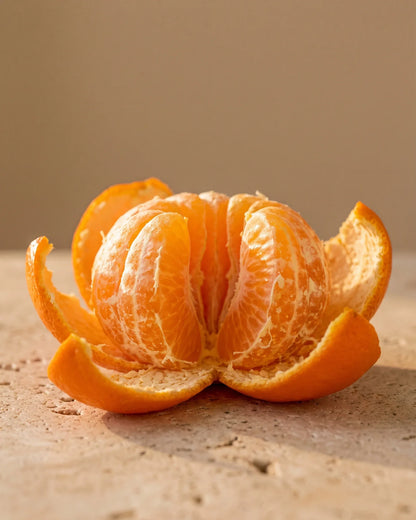 Una mandarina recién pelada con sus gajos brillando bajo una luz cálida: el aroma cítrico, dulce y jugoso del Aceite esencial puro de mandarina de Delune