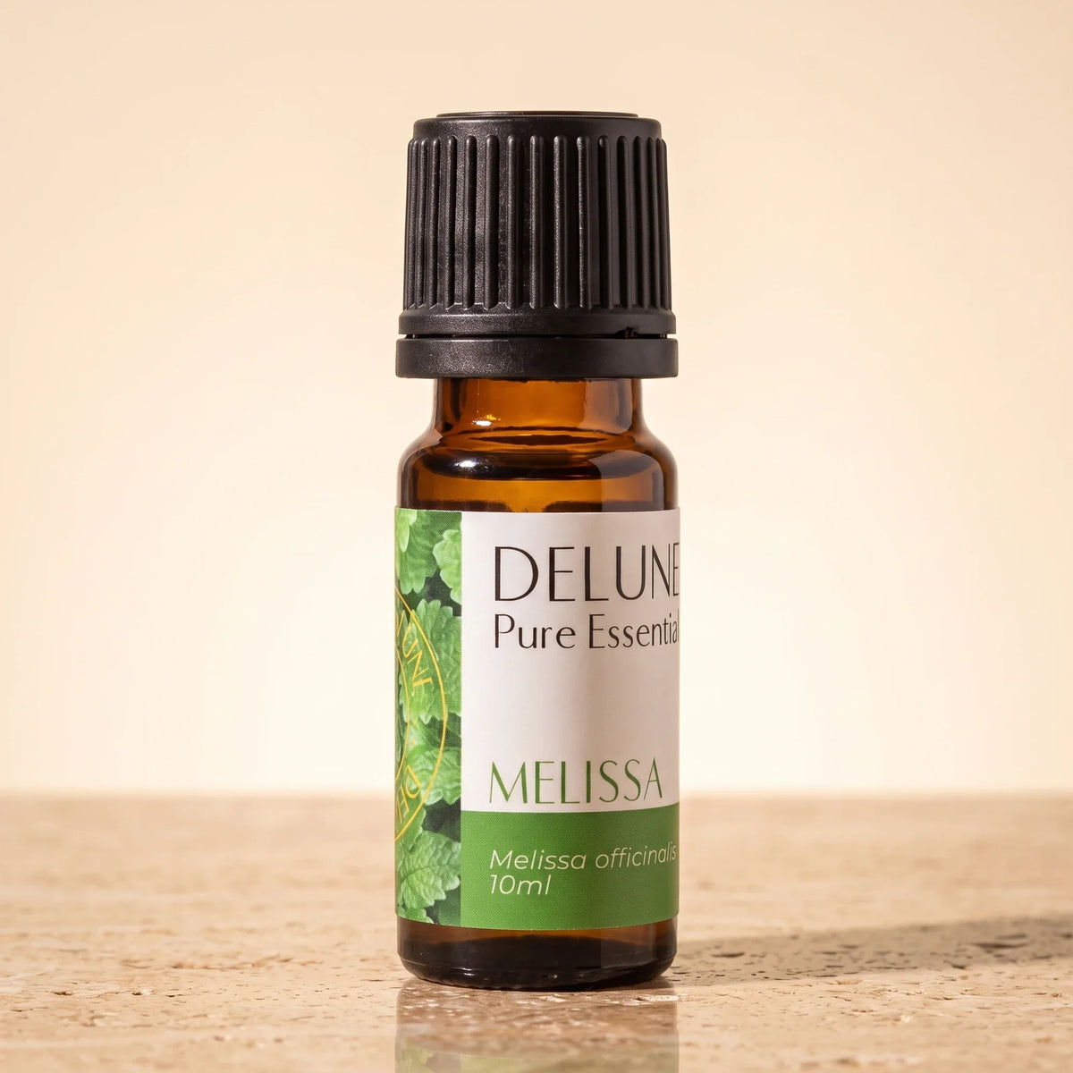 Aceite esencial puro de melisa de Delune en frasco de vidrio ámbar de 10 ml sobre piedra travertino cálida