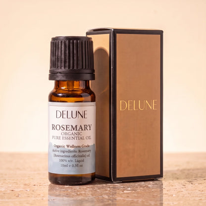 Aceite esencial de romero Organic Wellness Grade de Delune, frasco de vidrio ámbar de 10 ml con su caja de regalo Delune con detalles dorados, sobre piedra travertino cálida