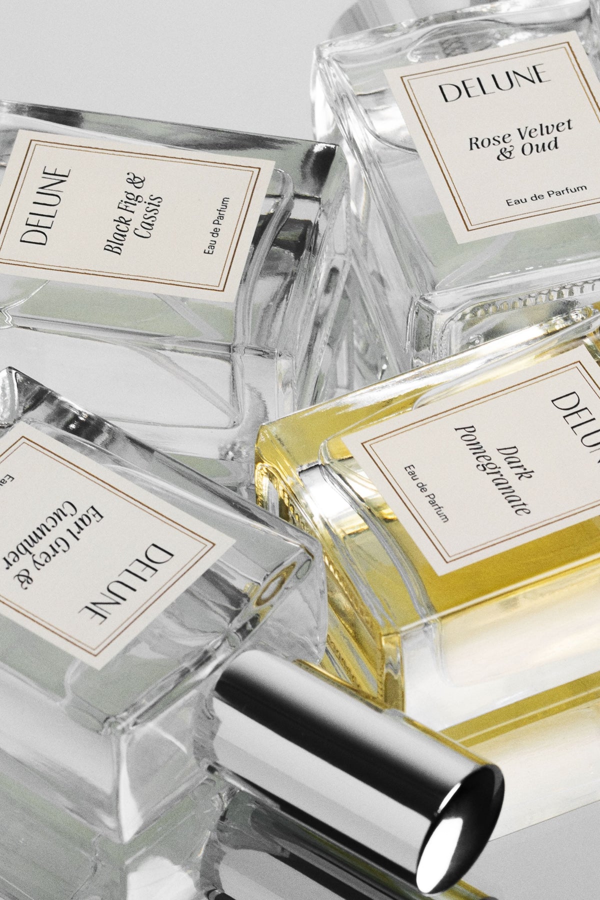 Primer plano de frascos de eau de parfum Delune, entre ellos Rose Velvet & Oud, con etiquetas color crema